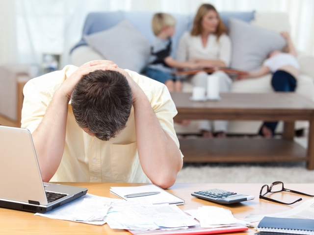 Man calculating his bills while his family are on the sofa